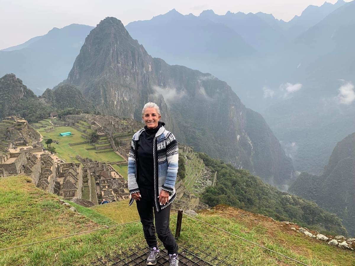 Armanda standing beside stone terraces with a steep green mountain behind her
