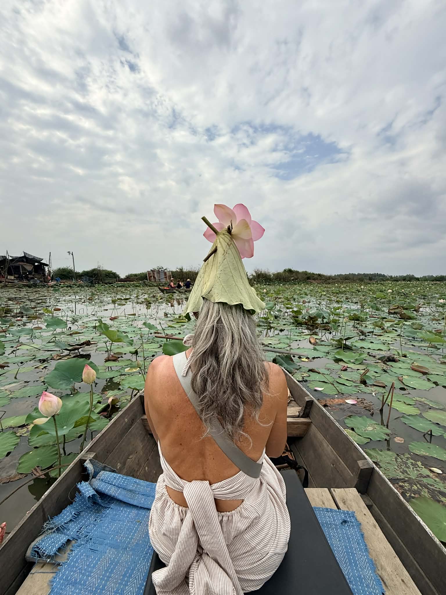 Armanda seated at the front of a wooden boat among lily pads with a pink flower above her head