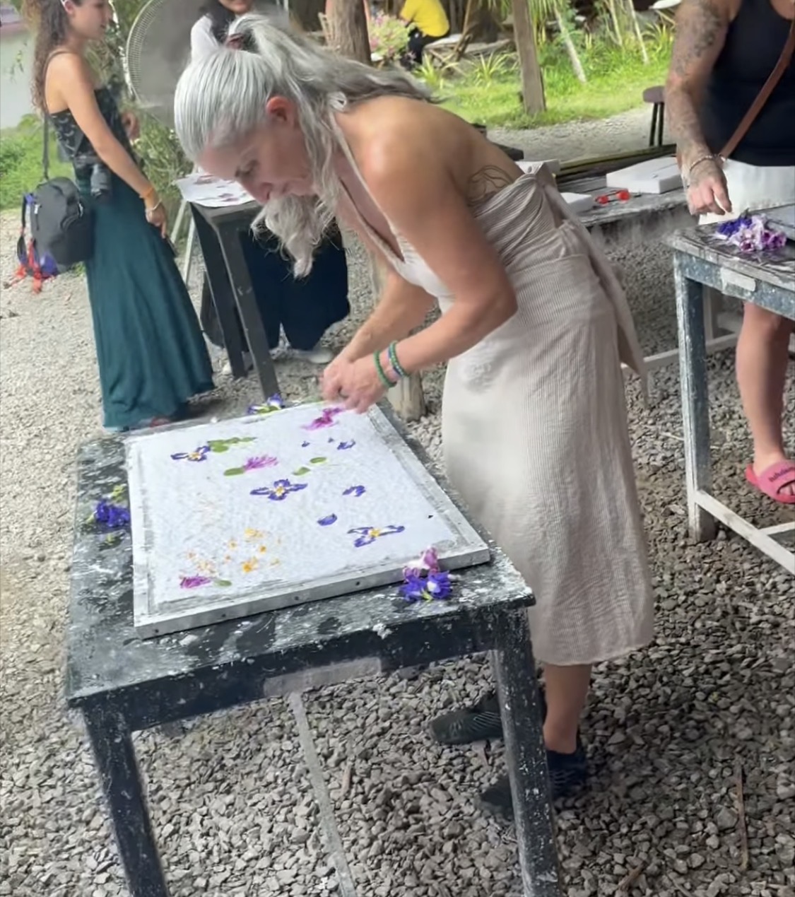 Armanda arranging colourful petals on a framed surface at an outdoor work table
