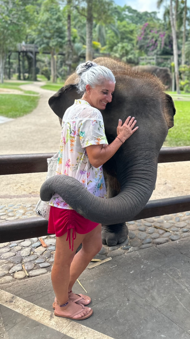 Armanda greeting an elephant with its trunk curved around her