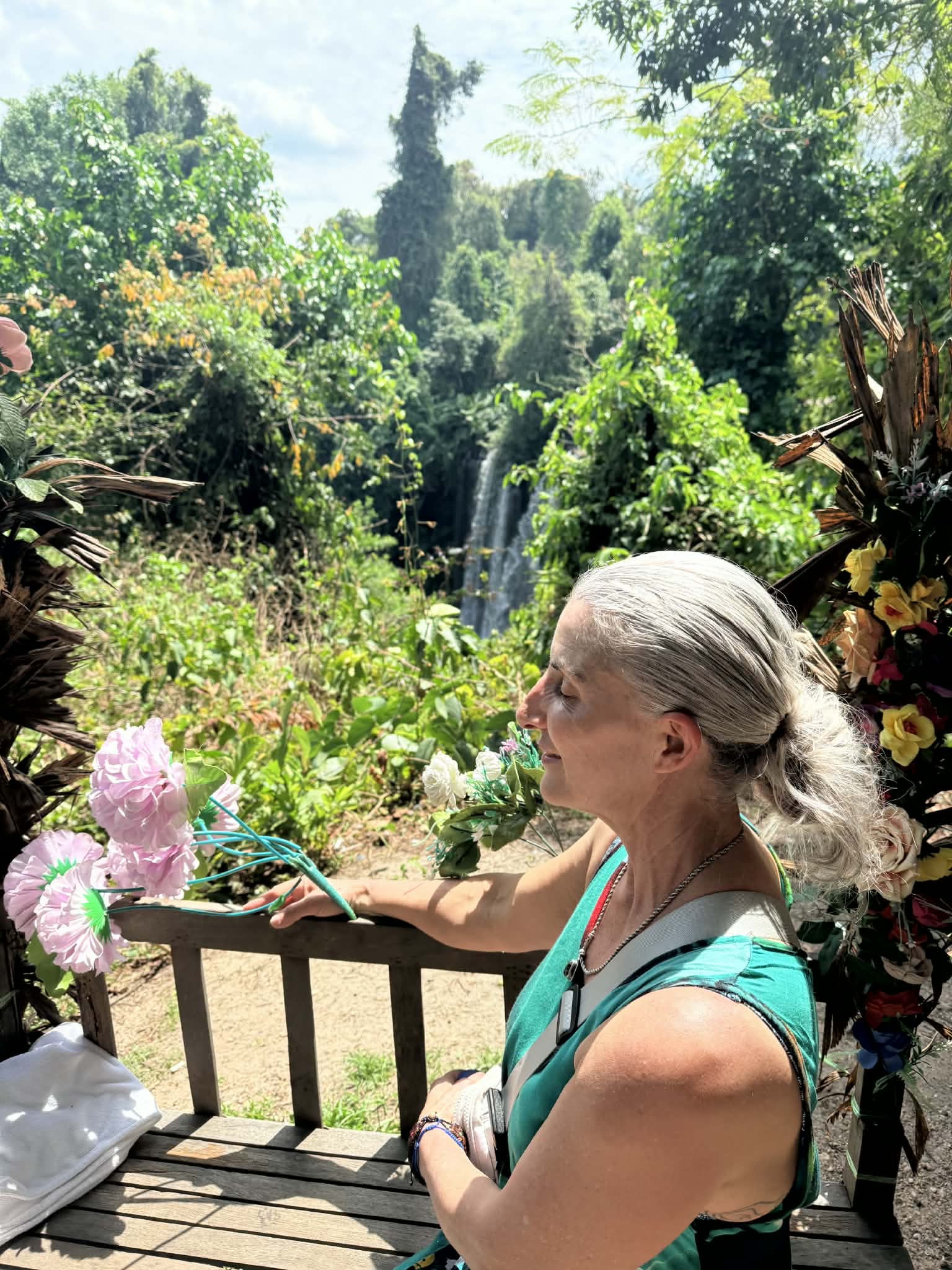 Armanda holding a small floral arrangement with her palms together beside a leafy garden
