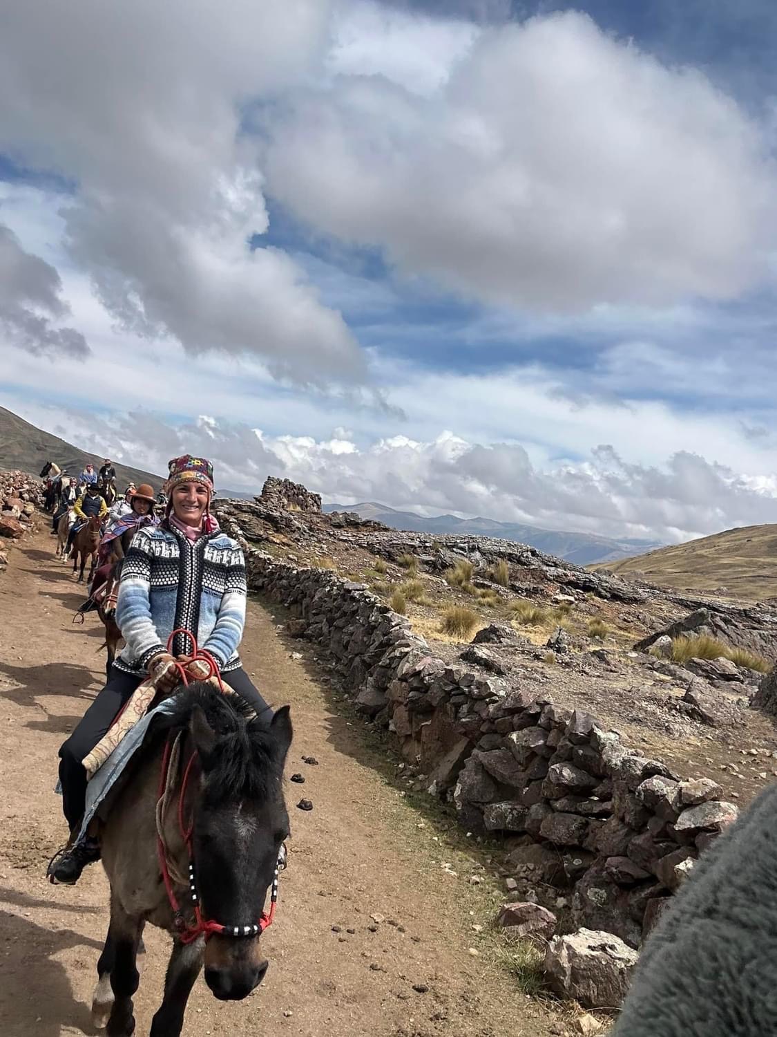 Armanda riding a horse along a rocky mountain path beneath clouds
