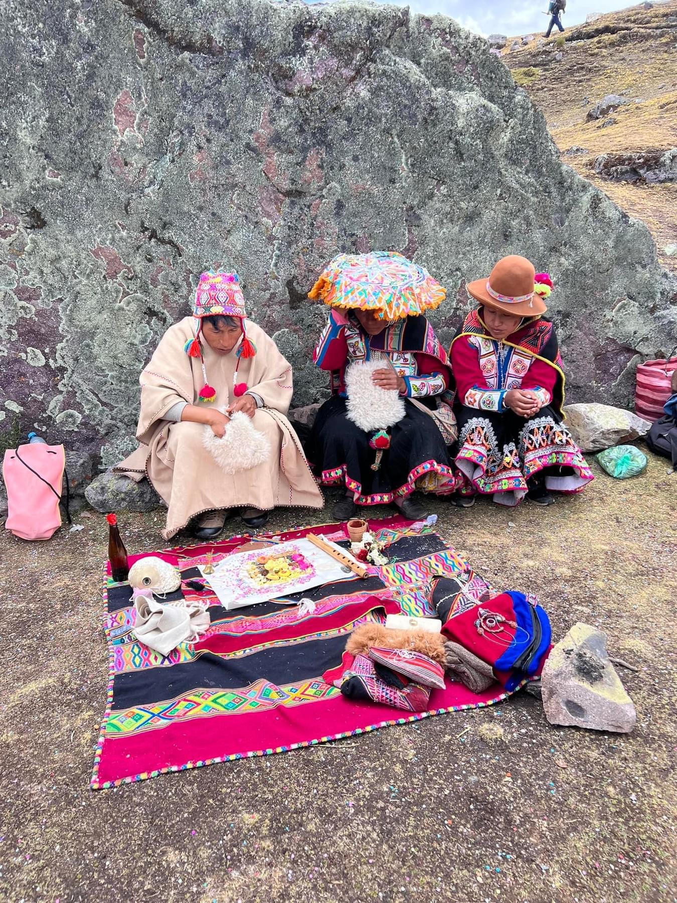 A small group seated behind a colourful ceremonial cloth beside a rock face