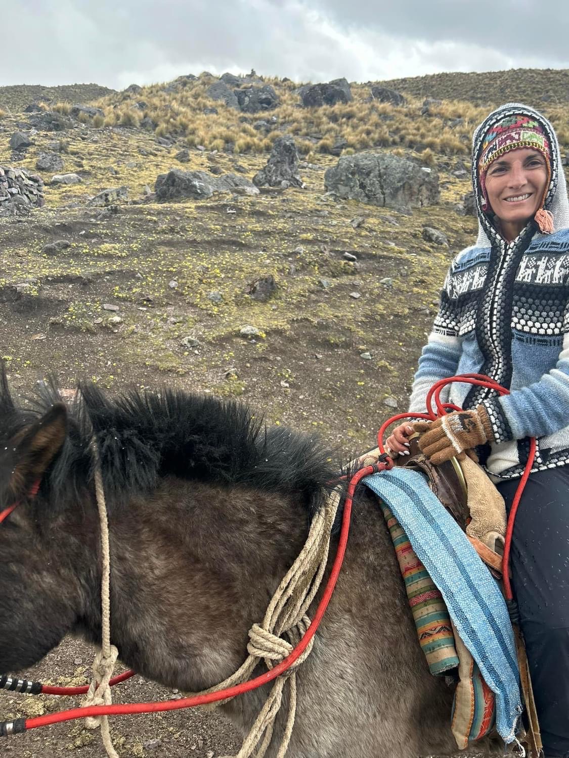 Armanda smiling while riding a horse on an open mountain trail