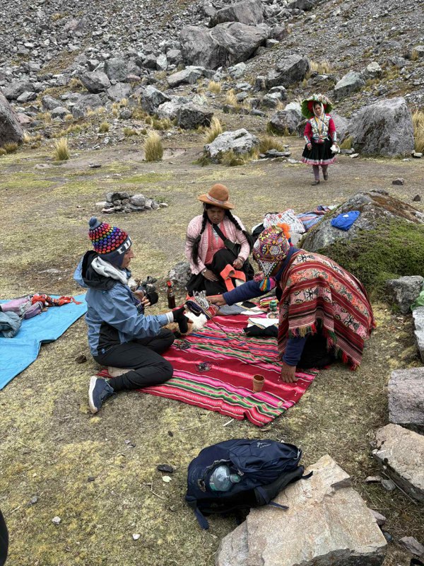 A small group gathered around a woven cloth in the mountains