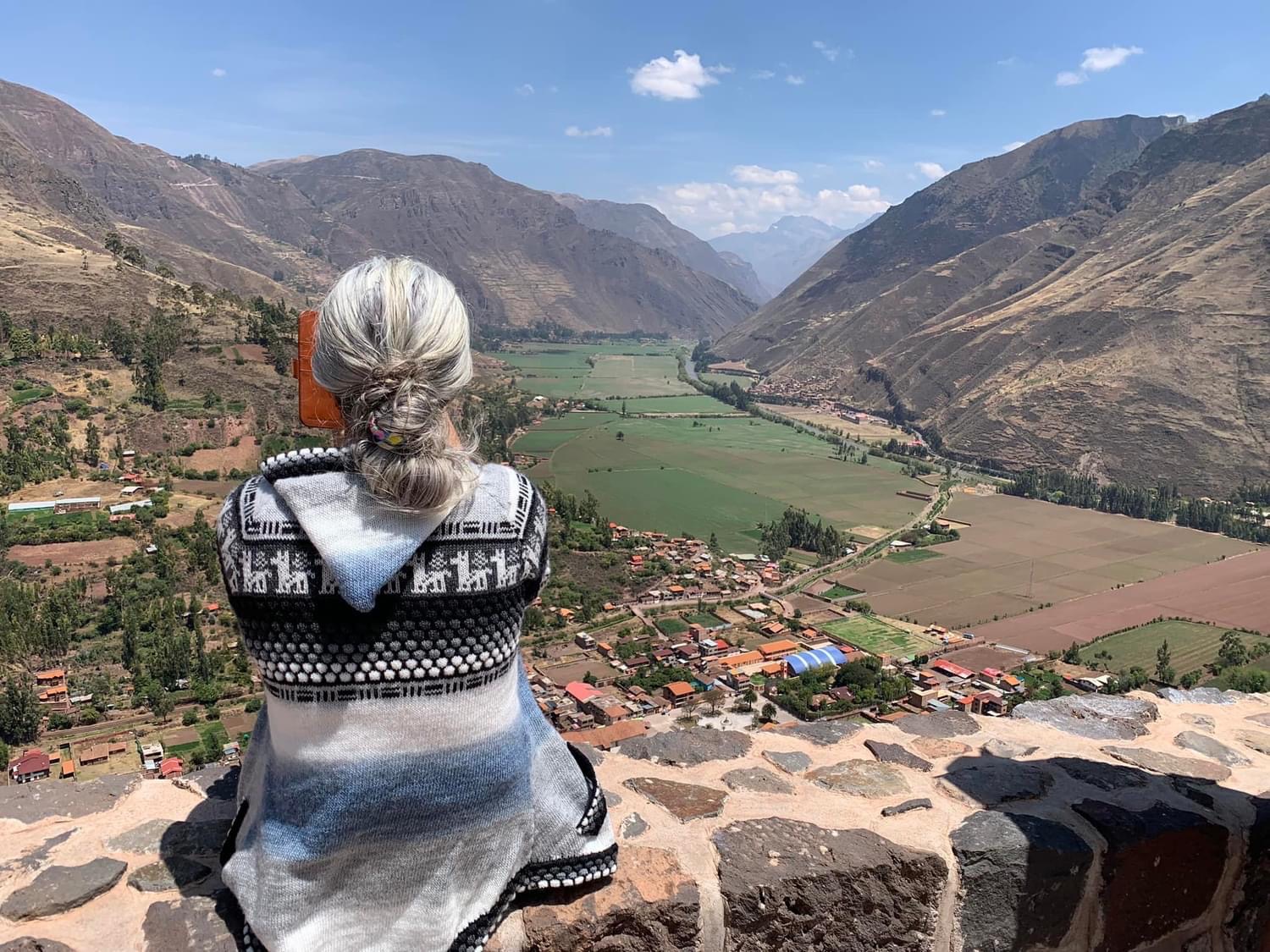 Armanda seated on a stone wall looking across a green valley between mountains