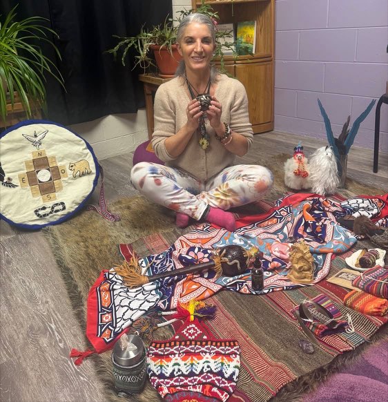 Armanda seated beside a drum and a collection of ceremonial objects