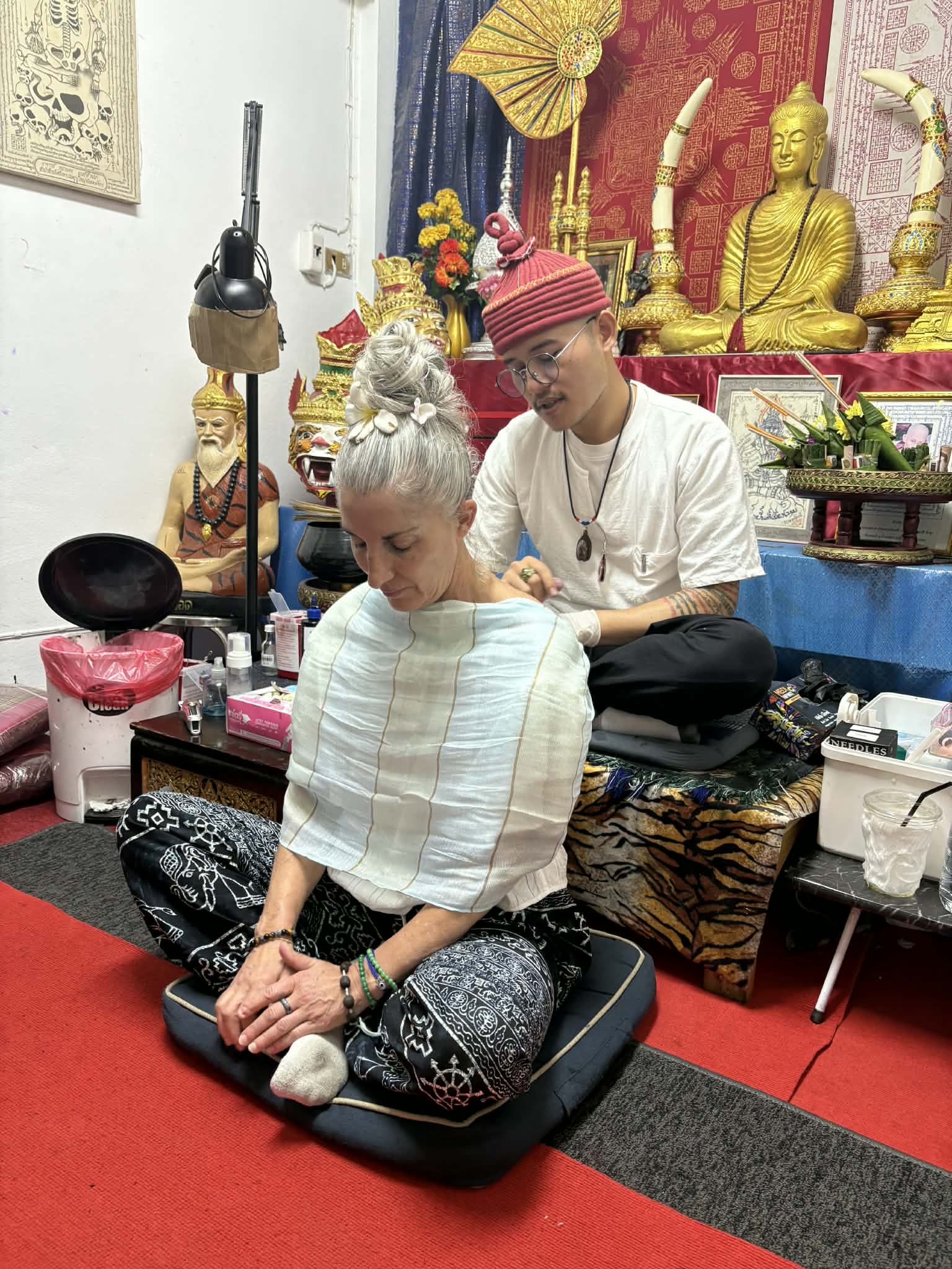 Armanda seated with her eyes closed while another person works behind her beside an ornate altar