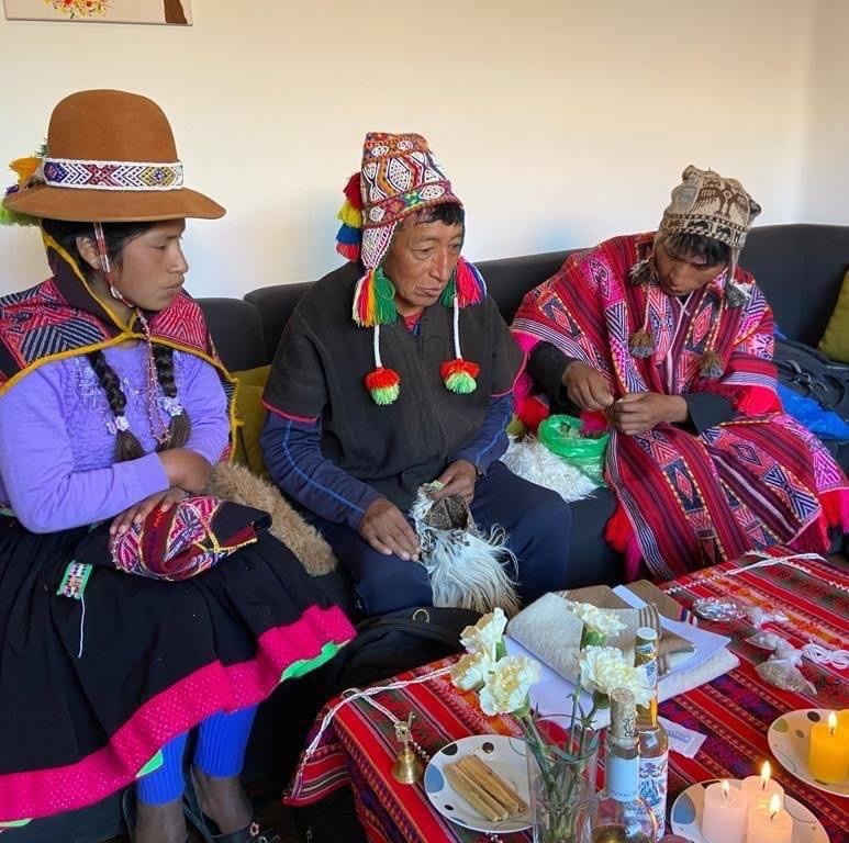 Armanda seated with two people in colourful woven clothing beside a ceremonial arrangement
