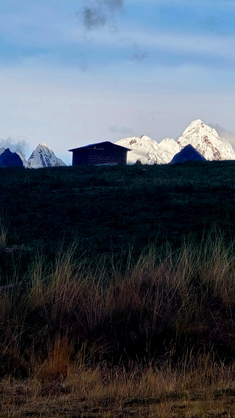 A dark hillside and a small building beneath distant snow-covered peaks