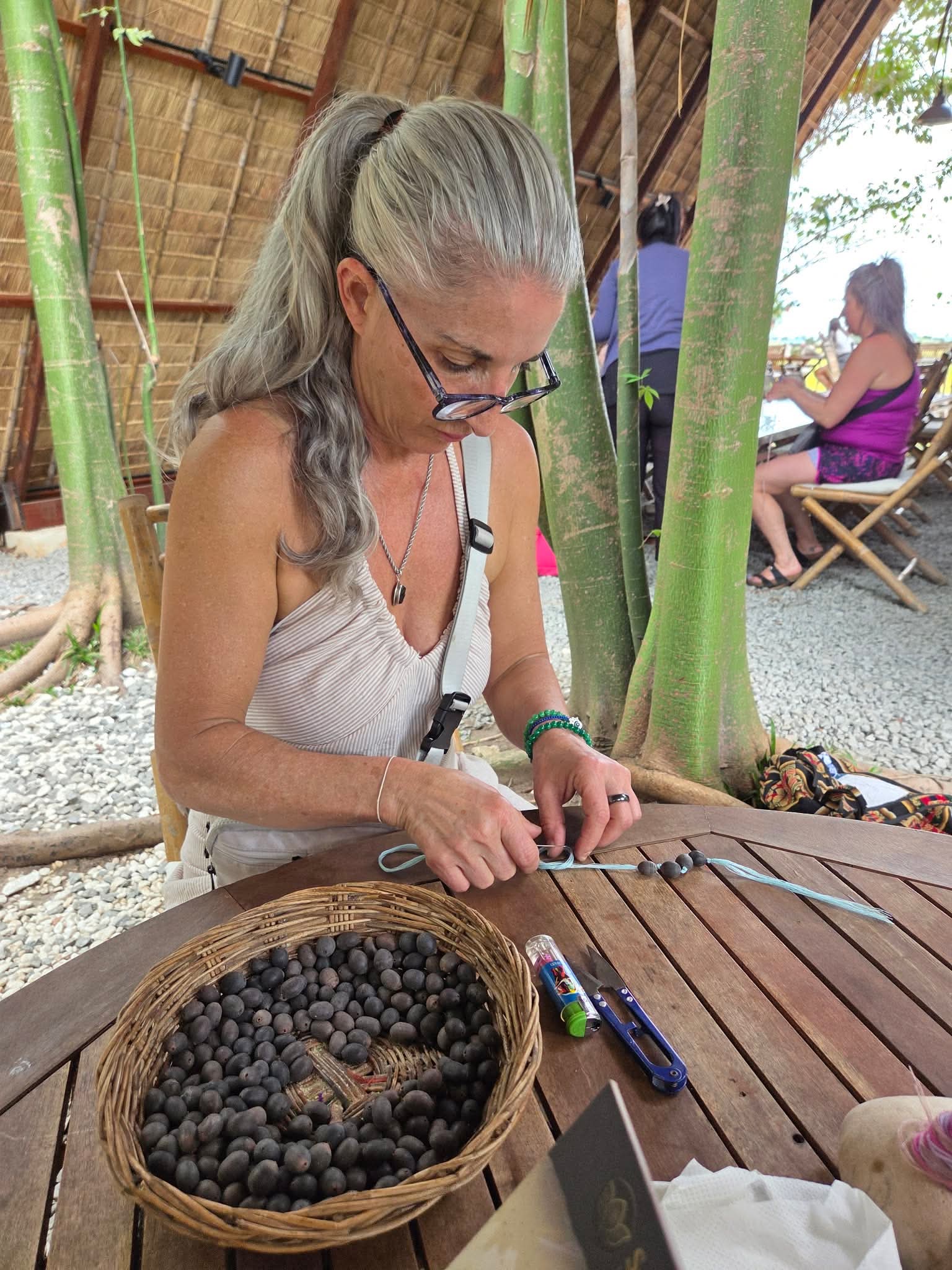 Armanda threading small dark beads onto a cord at a wooden table