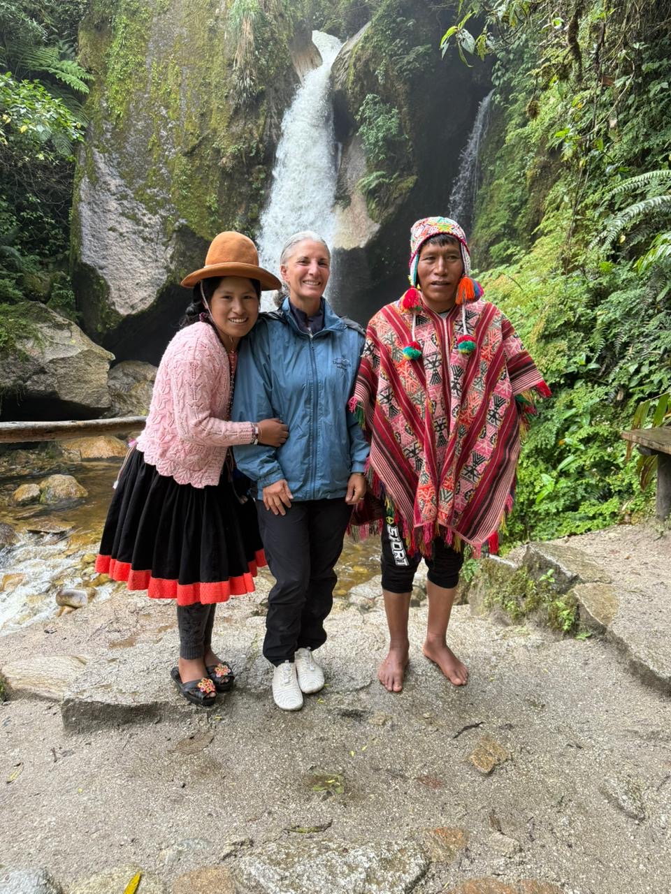 Three people standing together beside a waterfall
